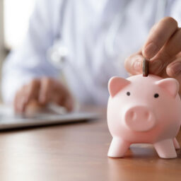 Close,Up,Young,Female,General,Practitioner,Putting,Coin,In,Piggy