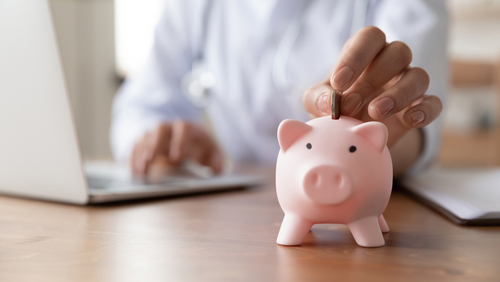 Close,Up,Young,Female,General,Practitioner,Putting,Coin,In,Piggy